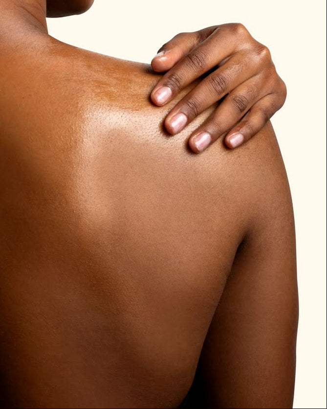 Close-up of a person's shoulder with another hand gently touching it against a neutral background